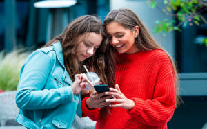 Duas jovens analisam conteúdos de infotenimento e marketing digital no smartphone, desenvolvidos pela Upplay.