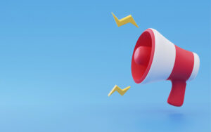 A imagem mostra um megafone, nas cores vermelha e branca. Ao redor dele, estão raios amarelos. O fundo da imagem é azul.