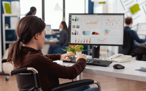 Em um ambiente corporativo, uma mulher presta atenção em um monitor do computador, que mostra diversos gráficos e dados.