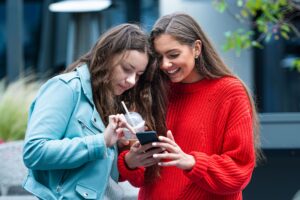 Duas jovens analisam conteúdos de infotenimento e marketing digital no smartphone, desenvolvidos pela Upplay.